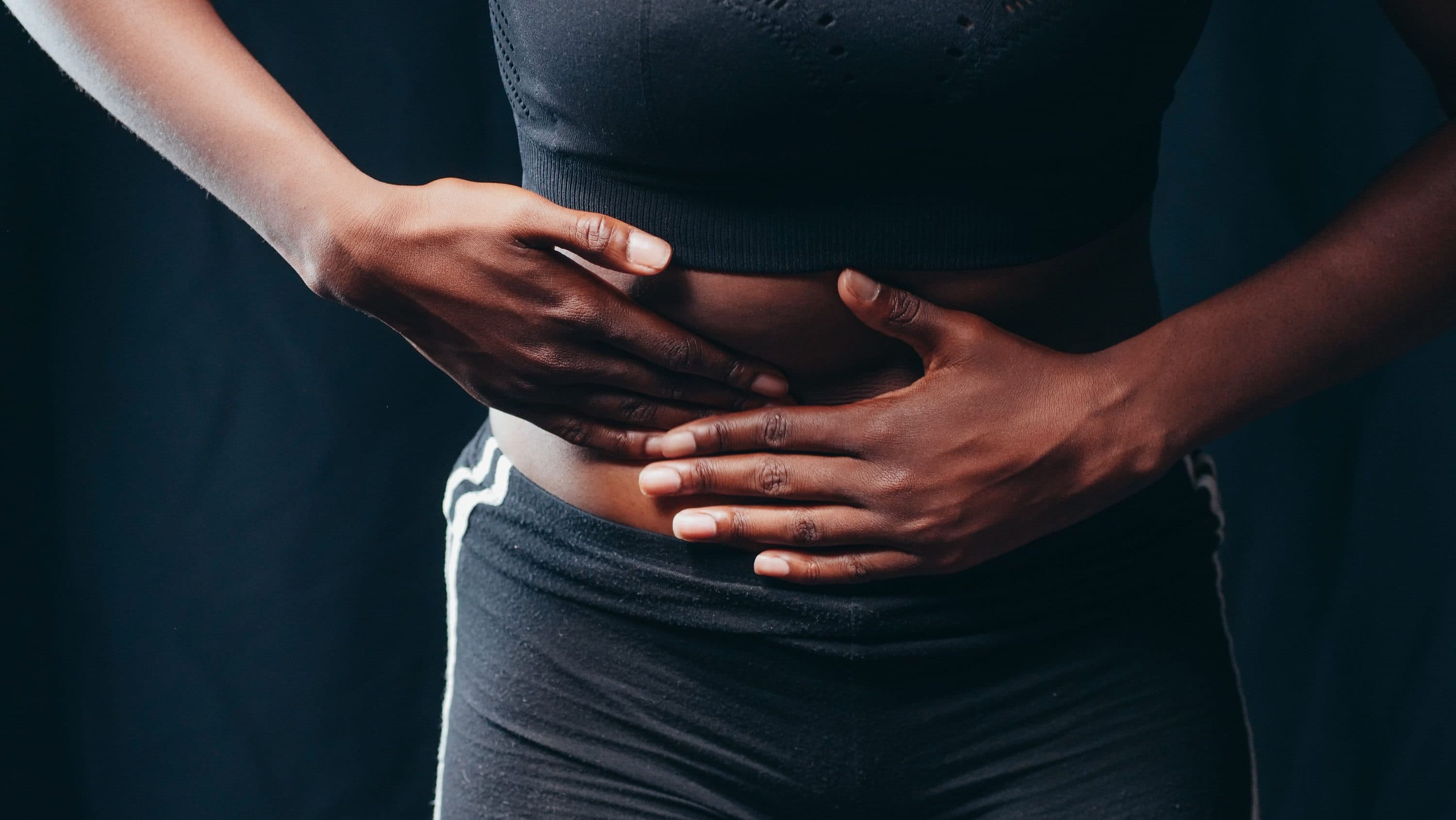 A woman’s hands resting over her stomach against a dark background